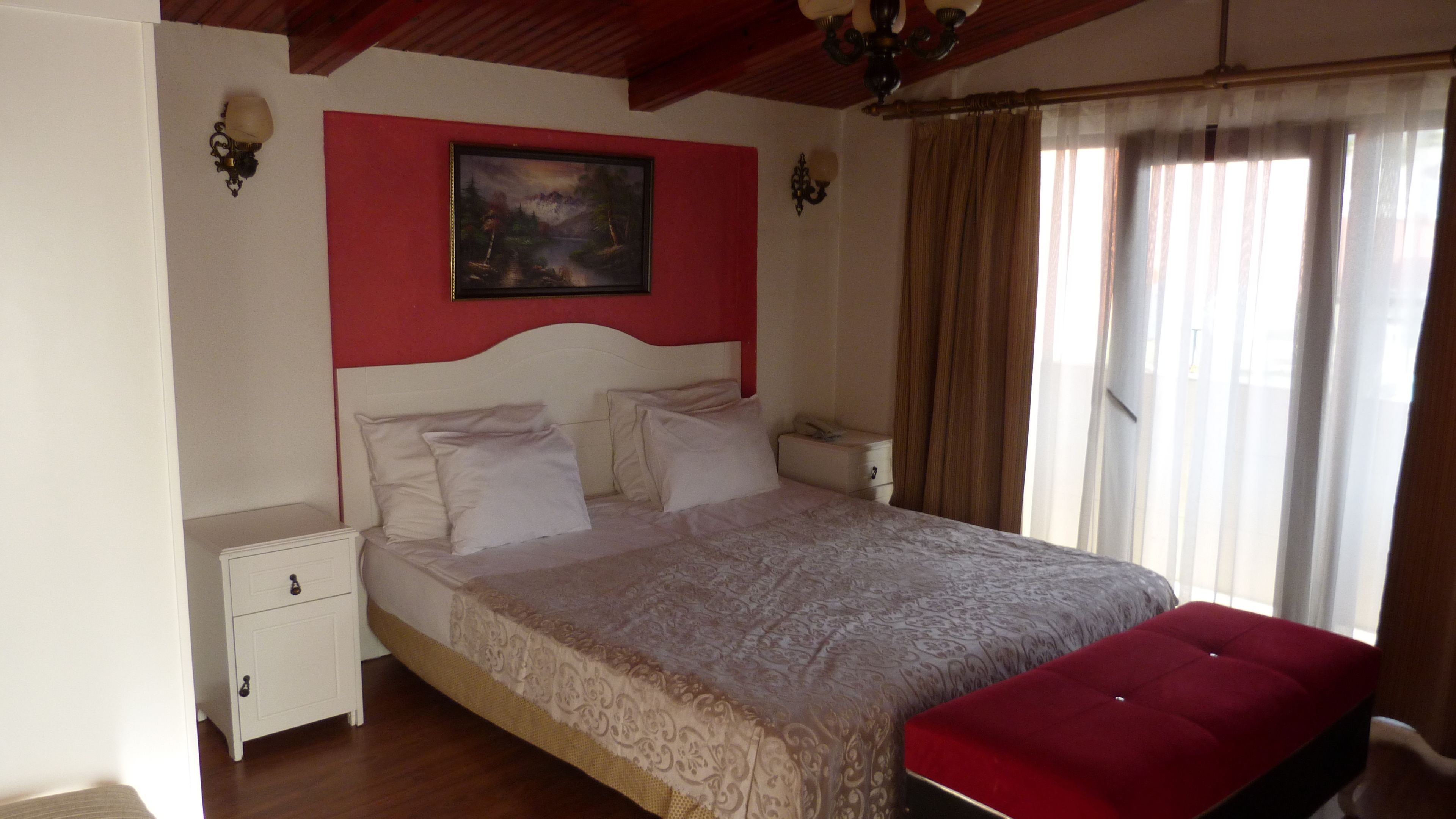 A bedroom with a large bed, a nightstand, a red bench, and a painting on the wall.