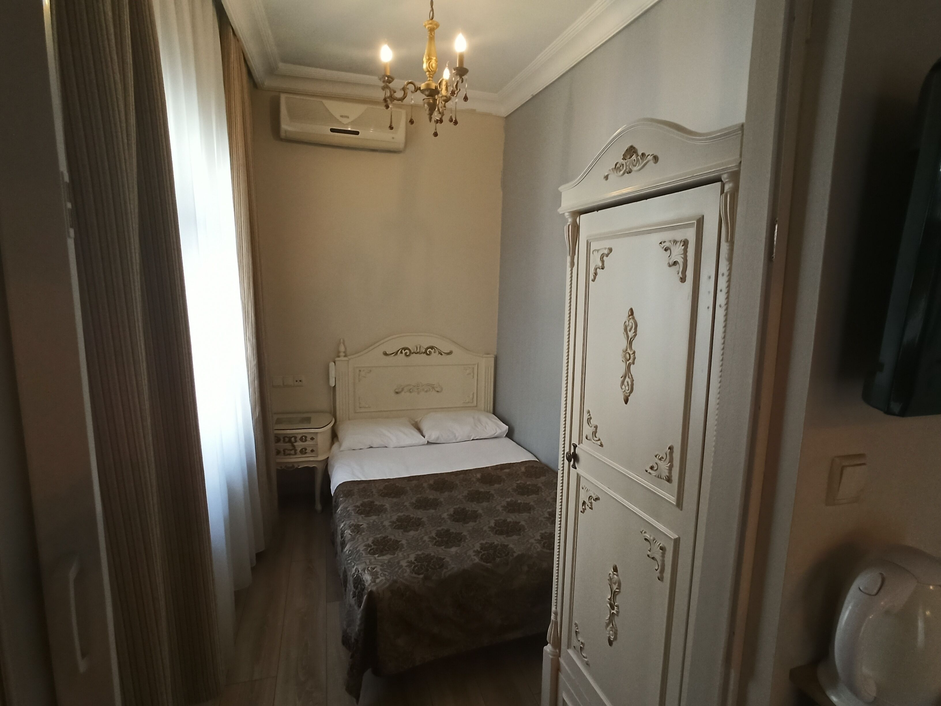 A bedroom with a bed, a wardrobe, a nightstand, an air conditioning unit, and a chandelier.