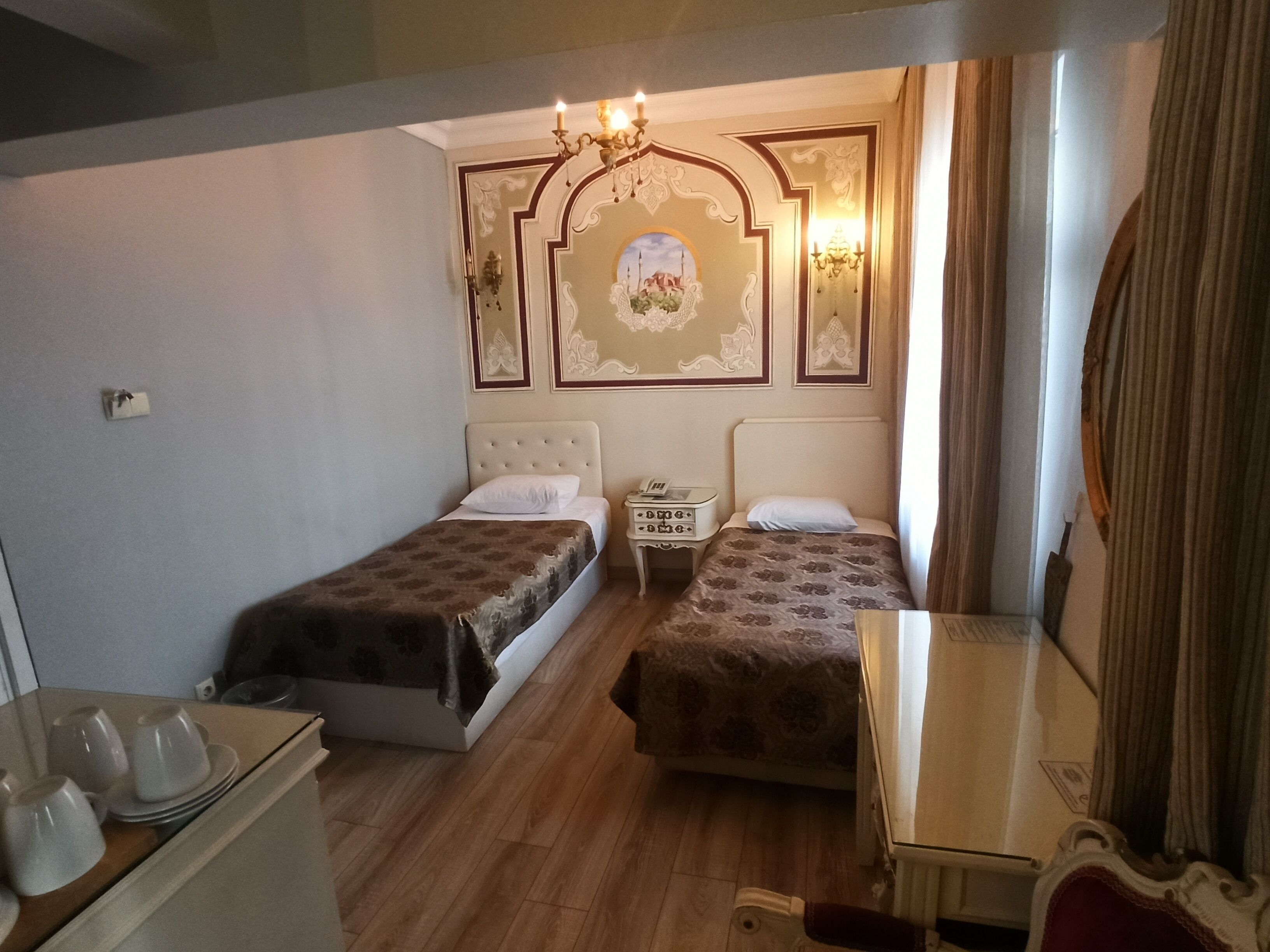 A hotel room with two beds, a small table, a nightstand, and a mirror.