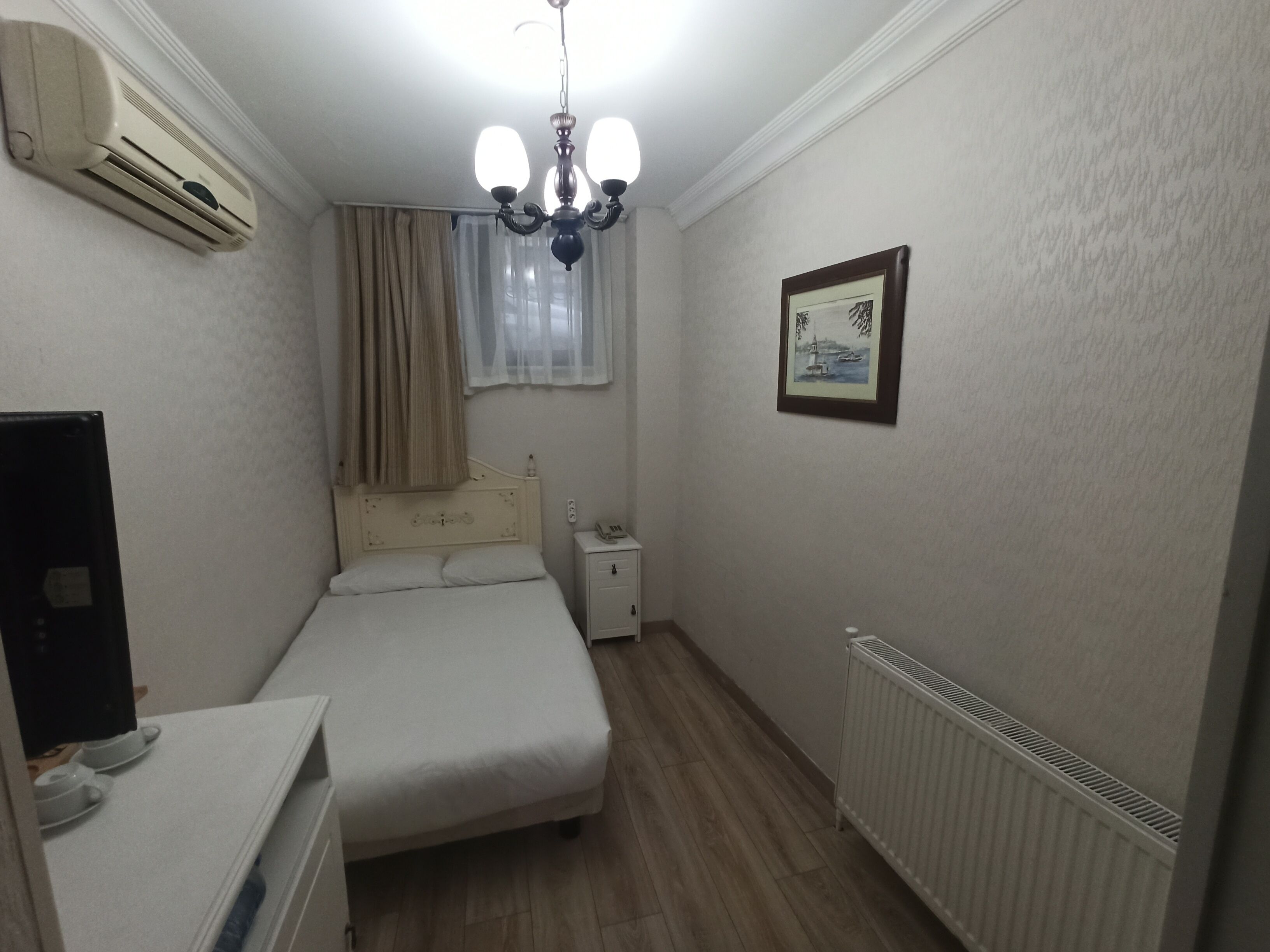 Une petite chambre à coucher, bien rangée, avec un lit, une table de chevet et un radiateur.
