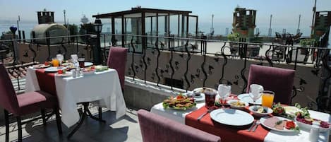 A rooftop dining area with tables set for breakfast, overlooking a scenic view of the sea.