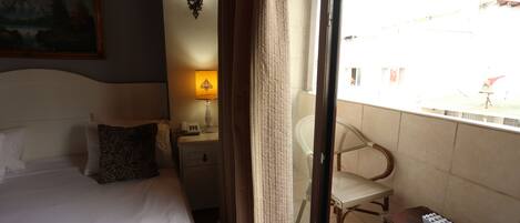 A hotel room with a bed, a nightstand with a lamp, a chair, and a small table with a remote control.