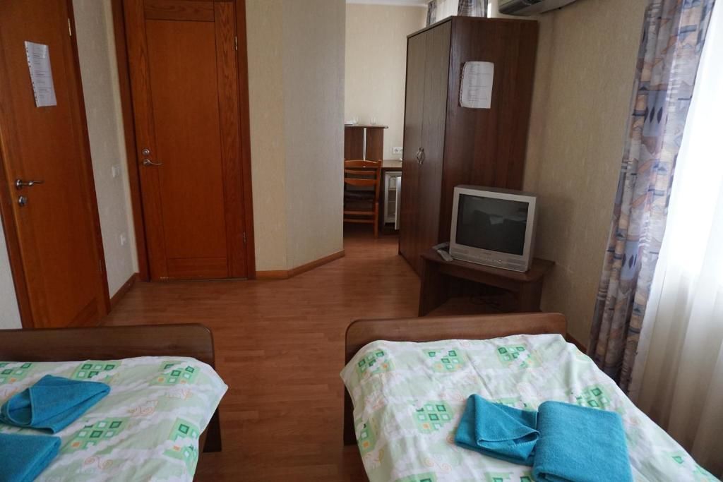 A hotel room with two beds, a wooden wardrobe, a television on a stand, and a small desk with a chair.
