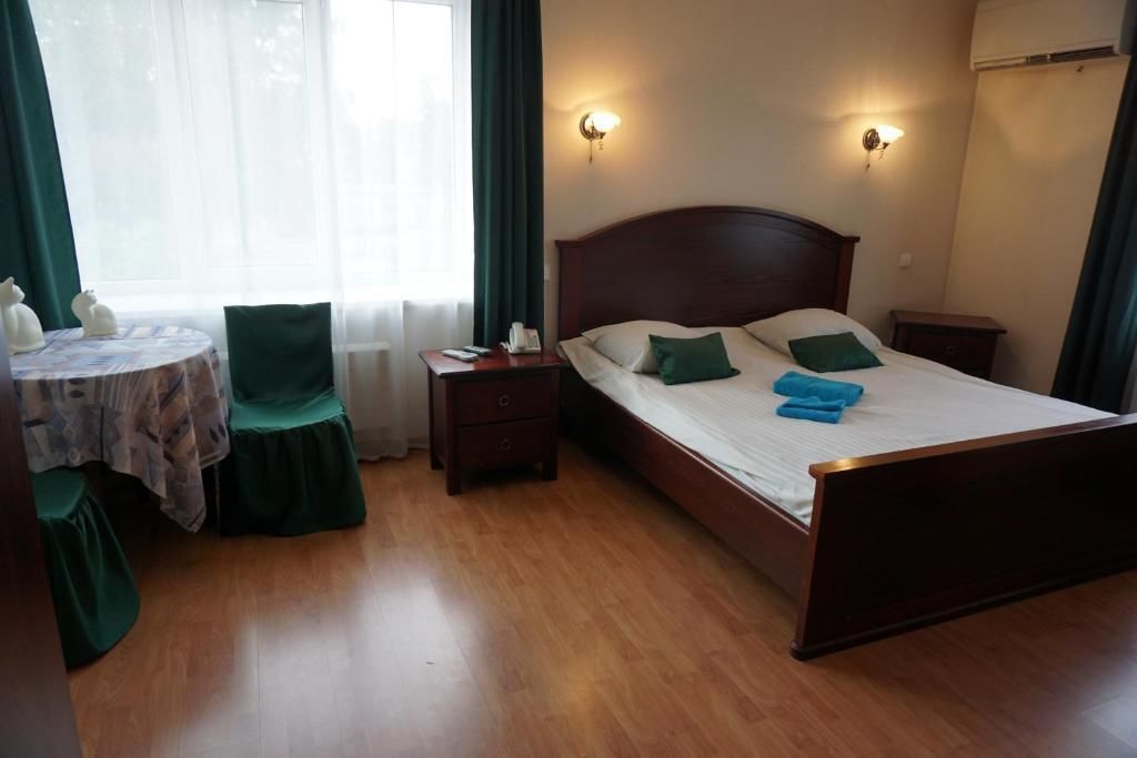 A hotel room with a wooden bed, two bedside tables, a small round table with a chair, and a window with curtains.