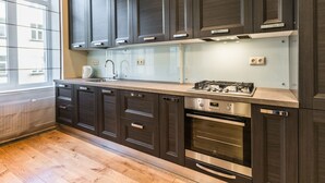 A modern kitchen with dark wood cabinets, stainless steel appliances, and a wooden floor. - Riga Lux Apartments - Ernesta (Riga)