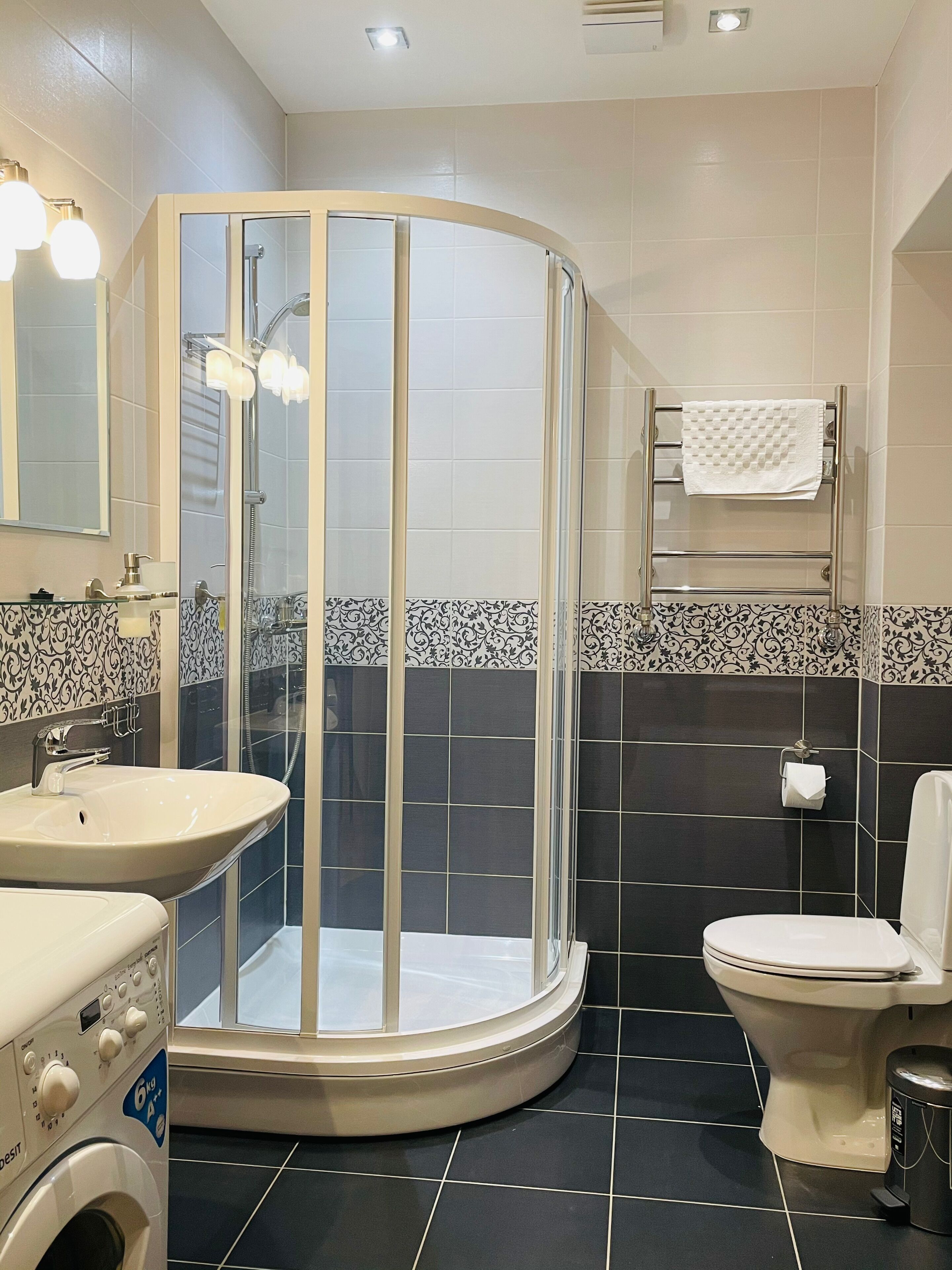 A bathroom with a glass-enclosed shower, a sink, a toilet, and a washing machine.
