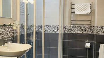 A bathroom with a glass-enclosed shower, a sink, a toilet, and a washing machine.