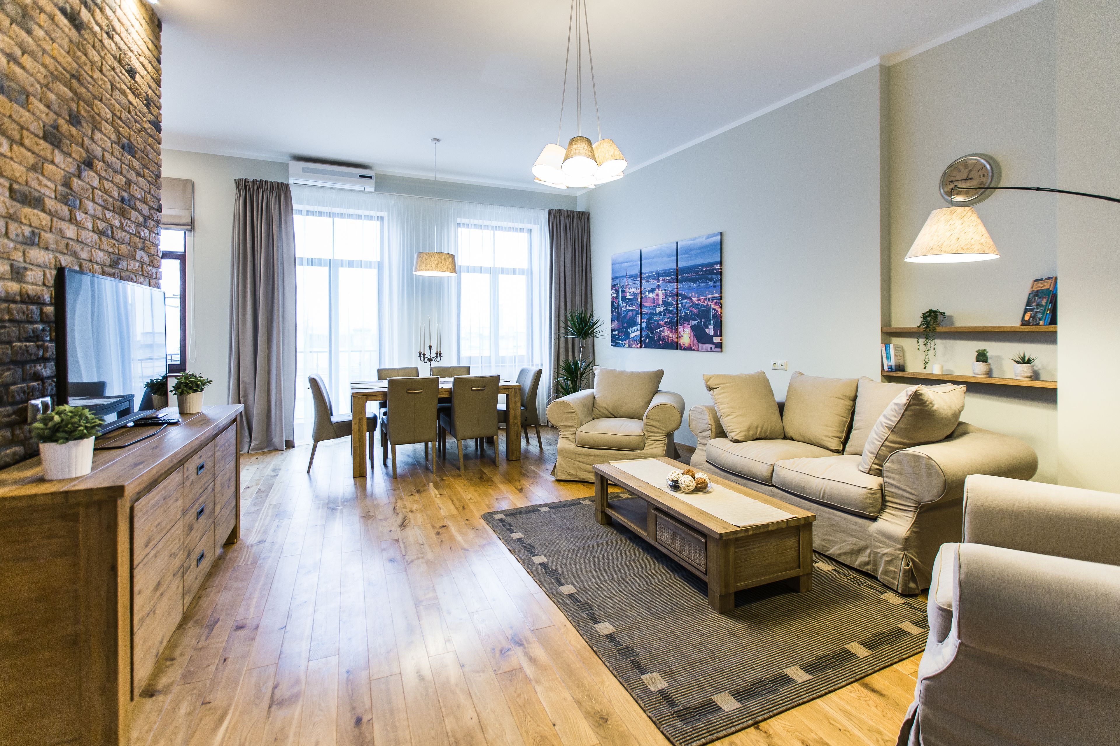 Moderni olohuone, jossa on puulattia, sohvaryhmä, ruokapöytä tuoleineen sekä keittiöalue, jossa on puinen työtaso ja kaapistot.