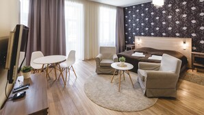 A modern hotel room with a large bed, two armchairs, a small table, a TV, and a desk with a computer and remote controls. - Riga Lux Apartments - Ernesta (Riga)