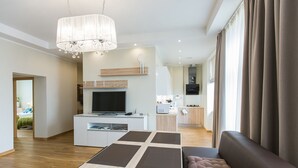 A modern living room with a sofa, a coffee table, and a TV. There is a kitchen area with a microwave and a refrigerator. - Riga Lux Apartments - Ernesta (Riga)