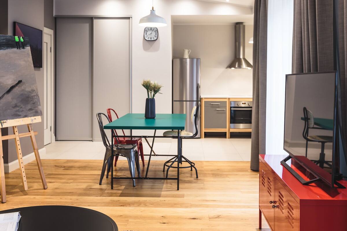 Ein modernes Wohnzimmer mit Esstisch, Stühlen, einem Fernseher und einer Küche im Hintergrund.