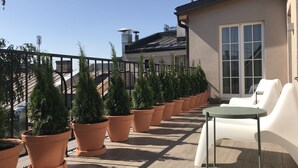 A rooftop terrace with potted plants, a white chair, and a table.