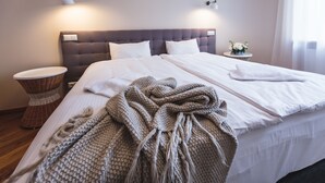 A neatly made bed with white linens, a grey knitted blanket, and a bedside table with a lamp.