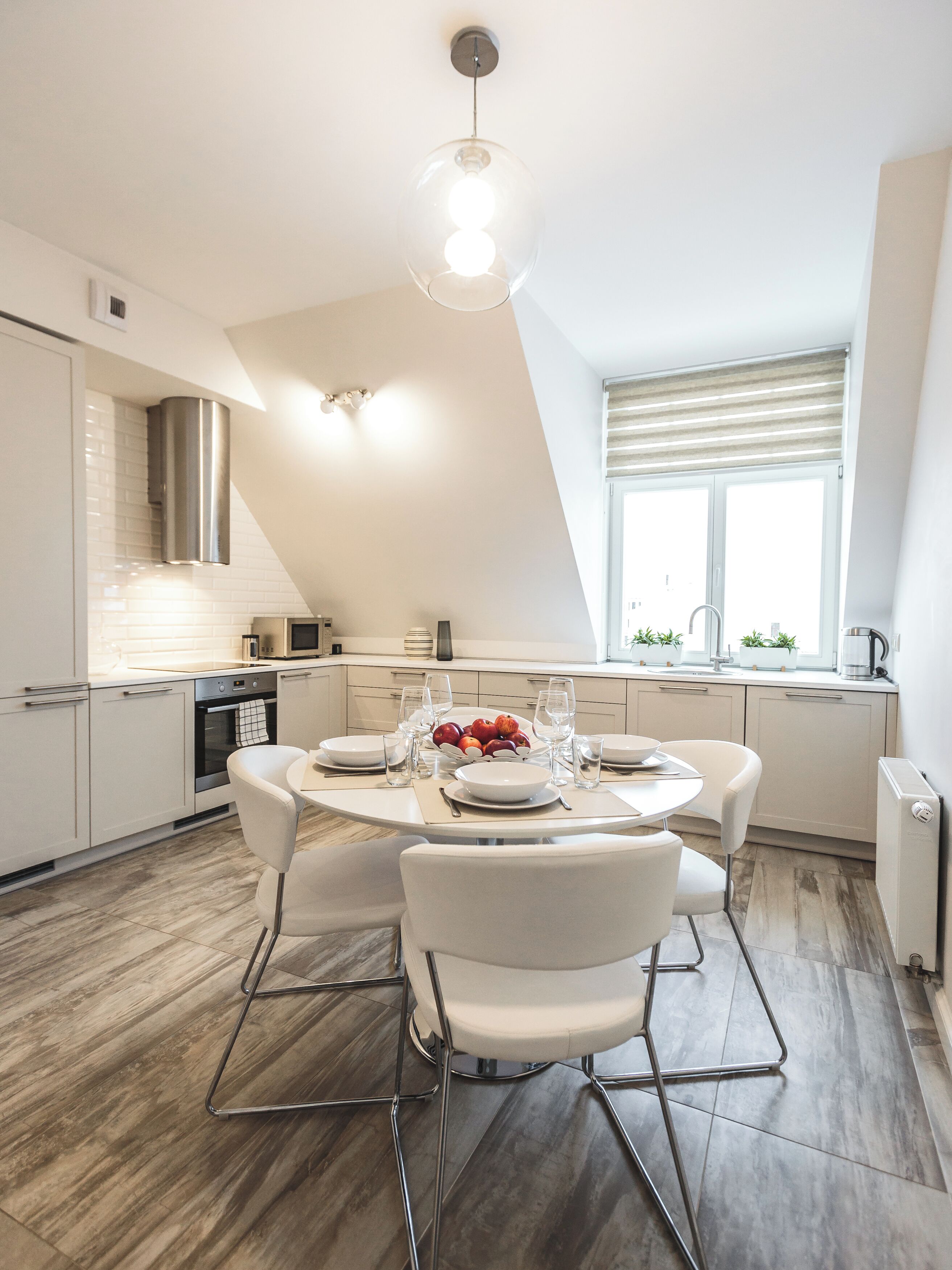 A modern kitchen with a dining area, featuring a round table, white chairs, and a fruit bowl.