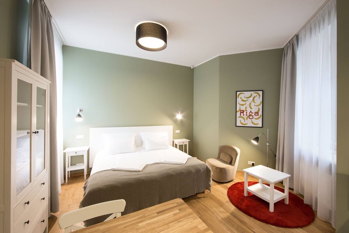 Ein Schlafzimmer mit einem Bett, Nachttischen, einem Sessel, einem Schreibtisch und einem Kleiderschrank.