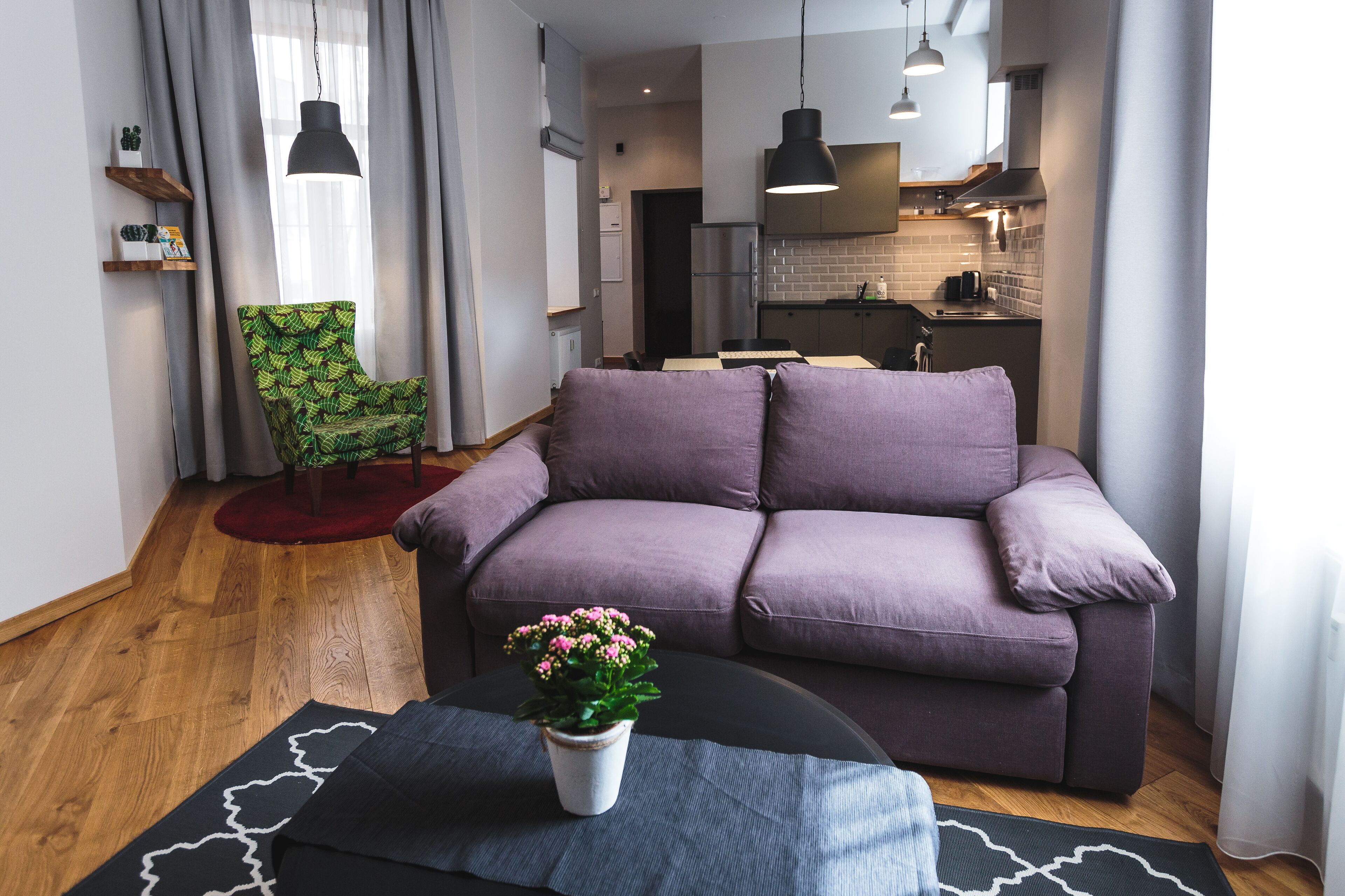 A modern living room with a purple sofa, a dining table, and a kitchen in the background.