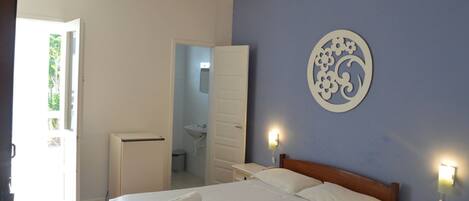 A bedroom with a bed, bedside tables, a wall-mounted light, and a door leading to a bathroom.