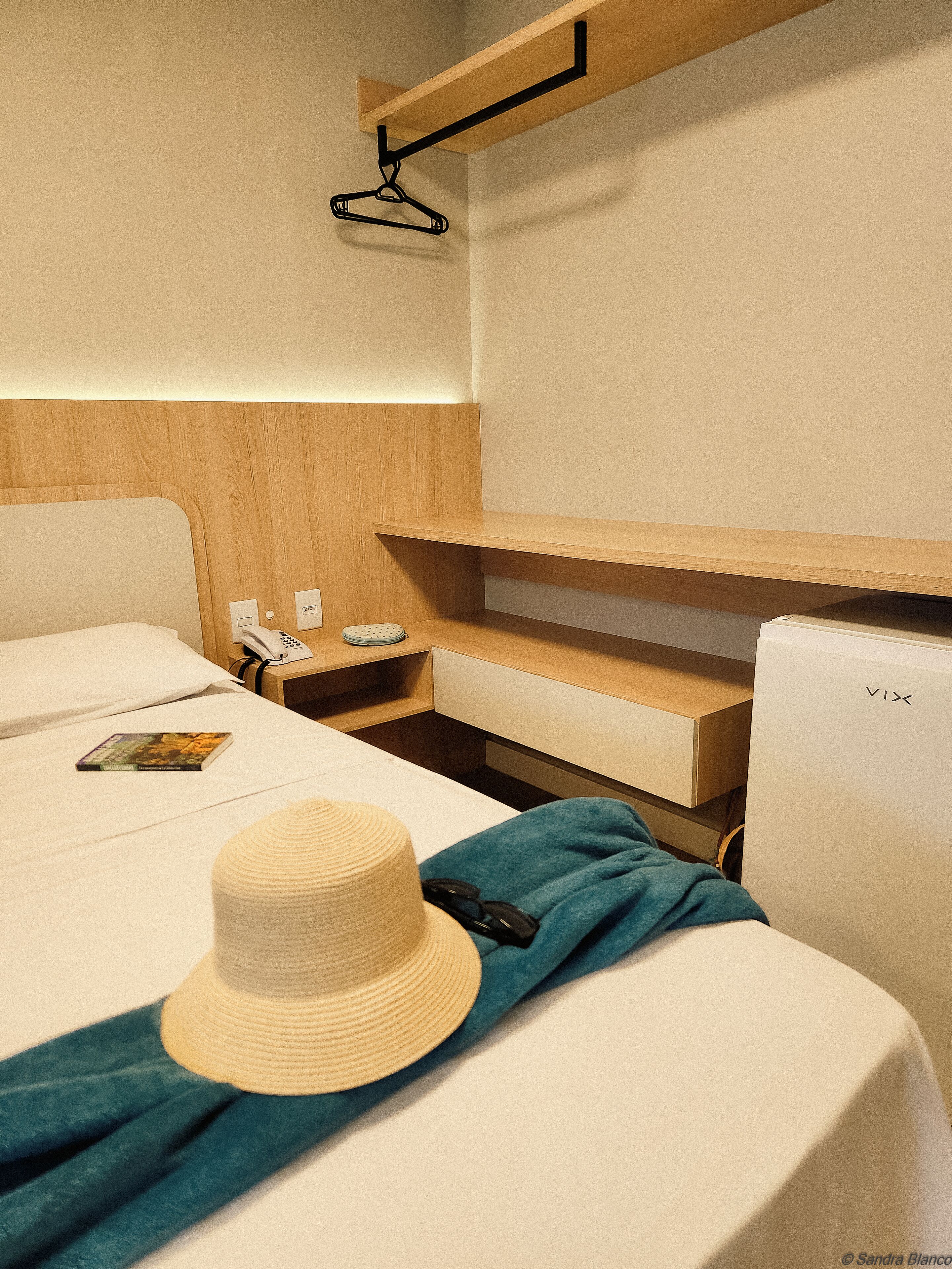 Una habitación de hotel con una cama, una mesita de noche con teléfono, un refrigerador VIX y un perchero.