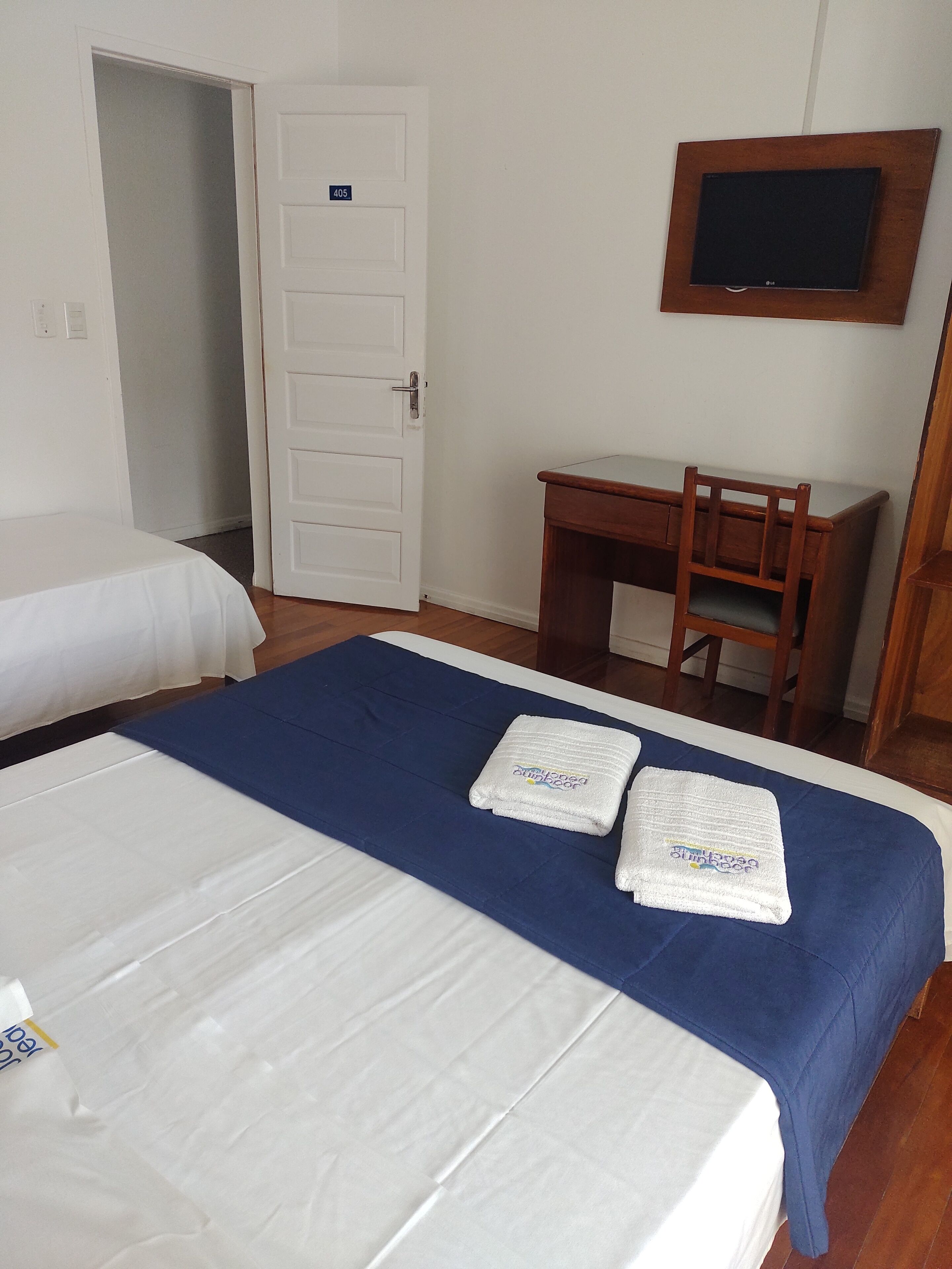 Habitación de hotel con dos camas, un escritorio, un televisor y una puerta con un número.
