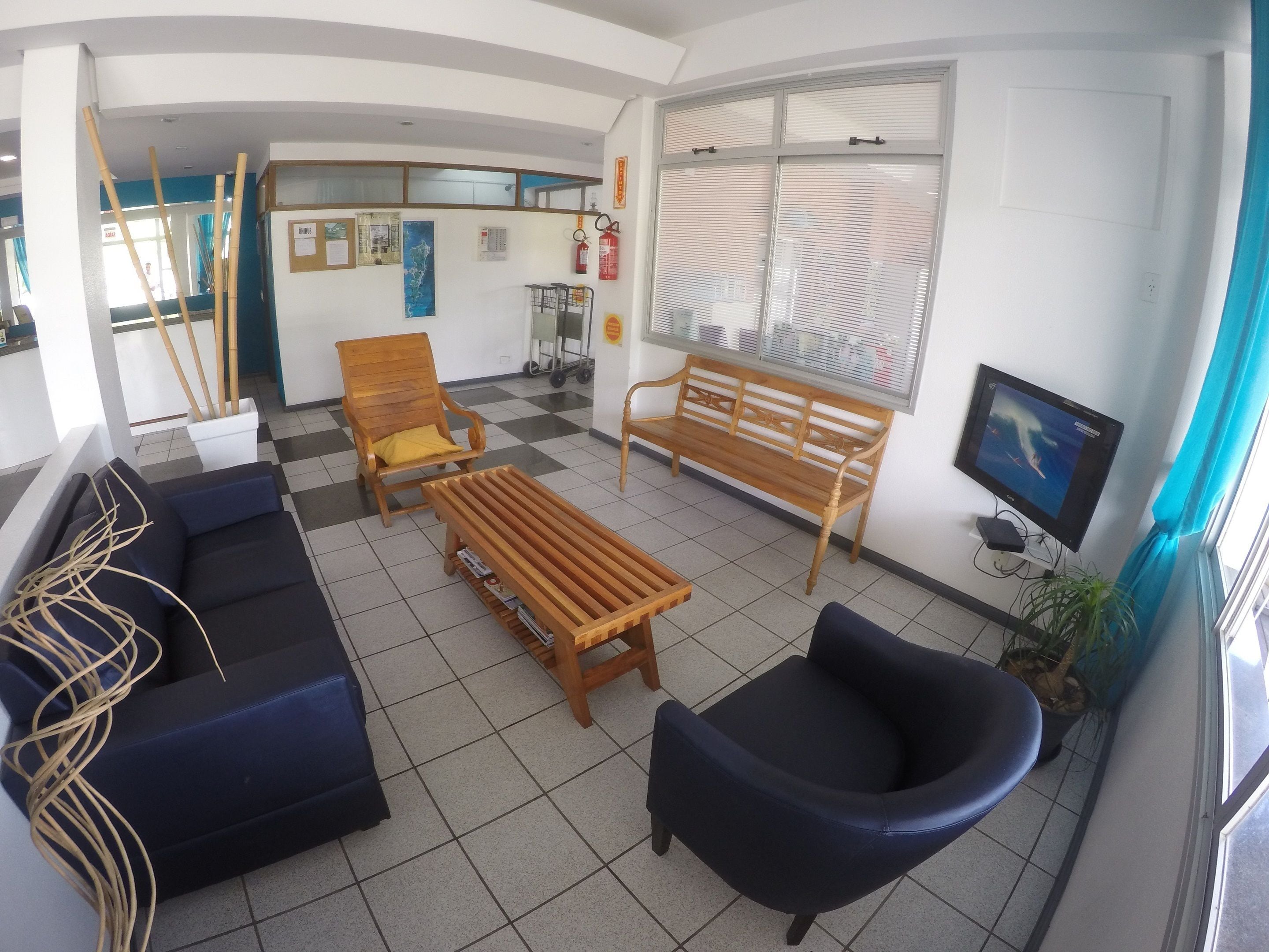 A lobby with a sofa, chairs, a wooden bench, a television, and a window with blinds.