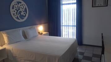 A hotel room with a large bed, a nightstand, a wall clock, and a window with curtains.
