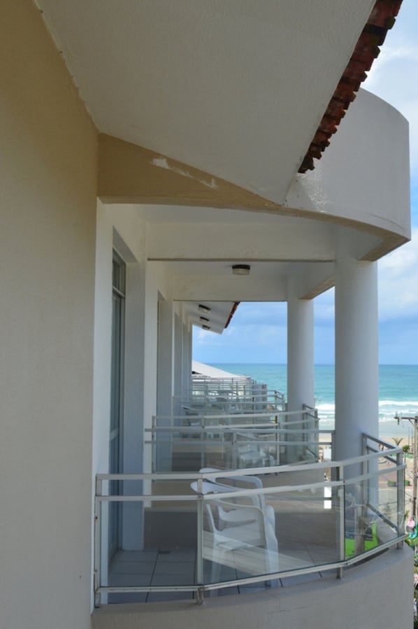 Un espacio al aire libre cubierto con barandilla de vidrio, una escalera que sube a un nivel superior y vistas al océano.