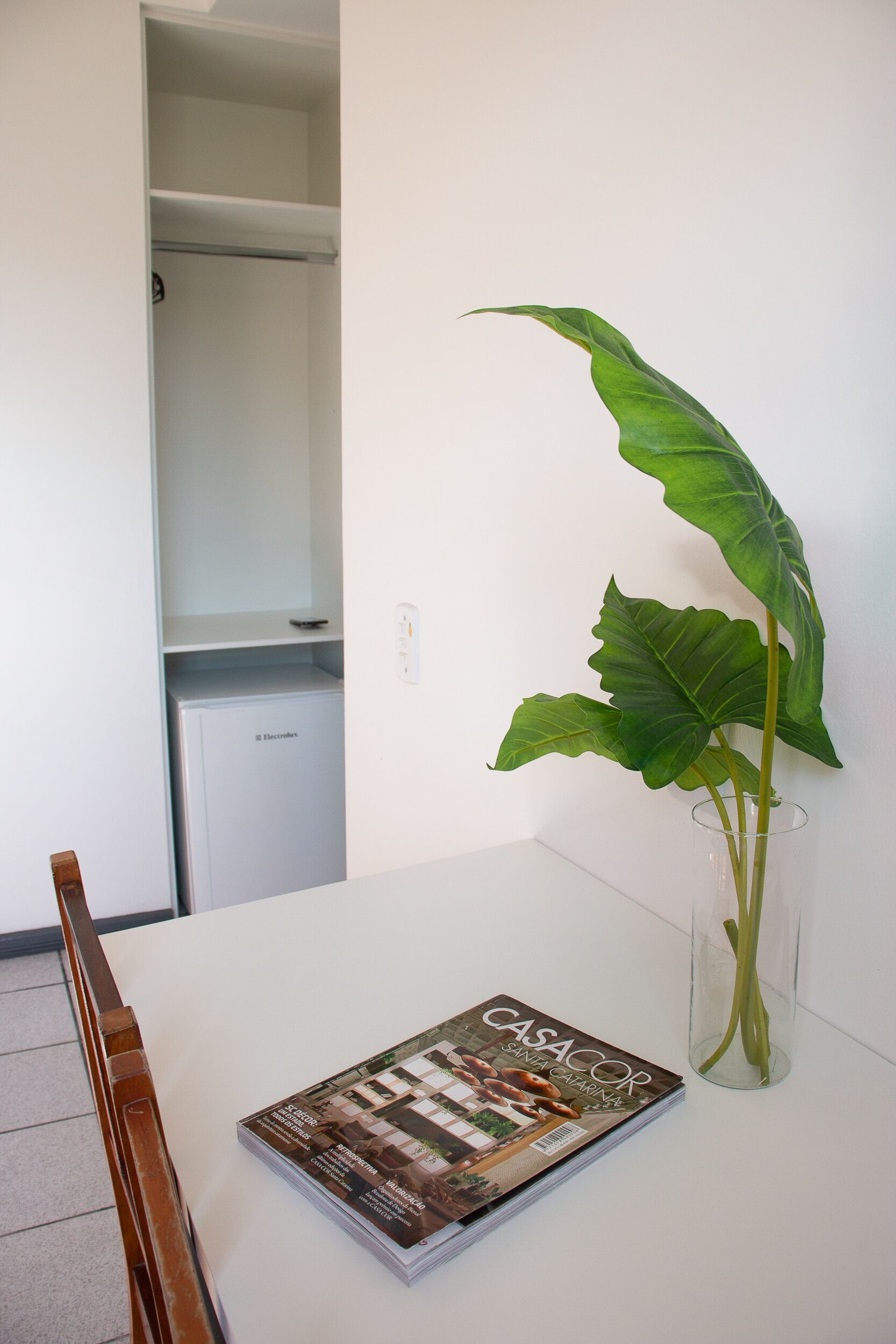 Une table blanche avec un magazine et un vase transparent contenant une plante.