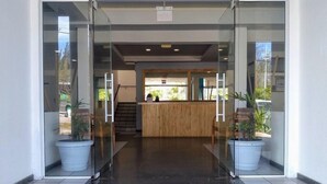 A hotel reception area with a wooden reception desk, glass doors, and potted plants.
