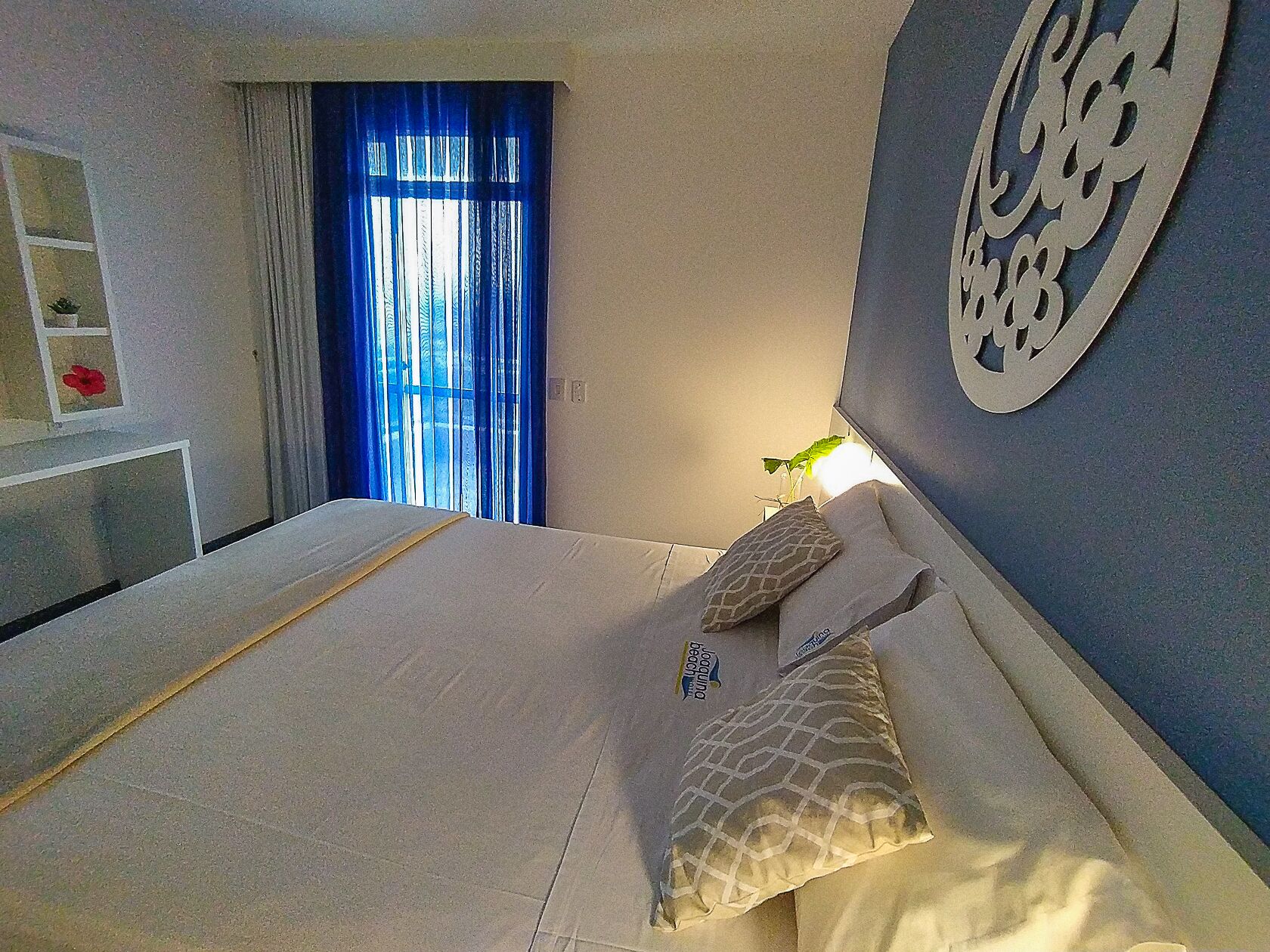 A bedroom with a bed, a nightstand, a wall clock, and a window with curtains.