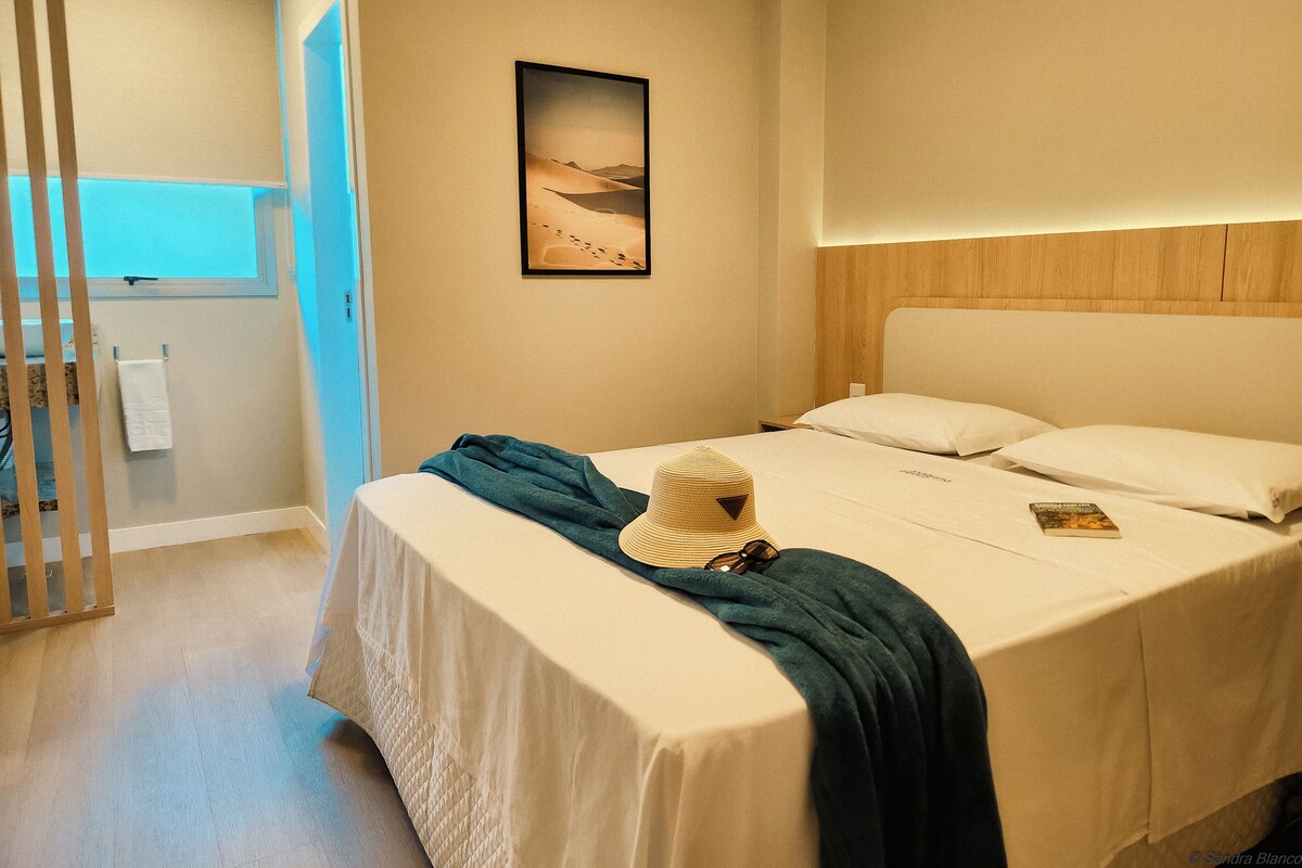 Een hotelkamer met een bed, een raam, een handdoekrek en een schilderij aan de muur.
