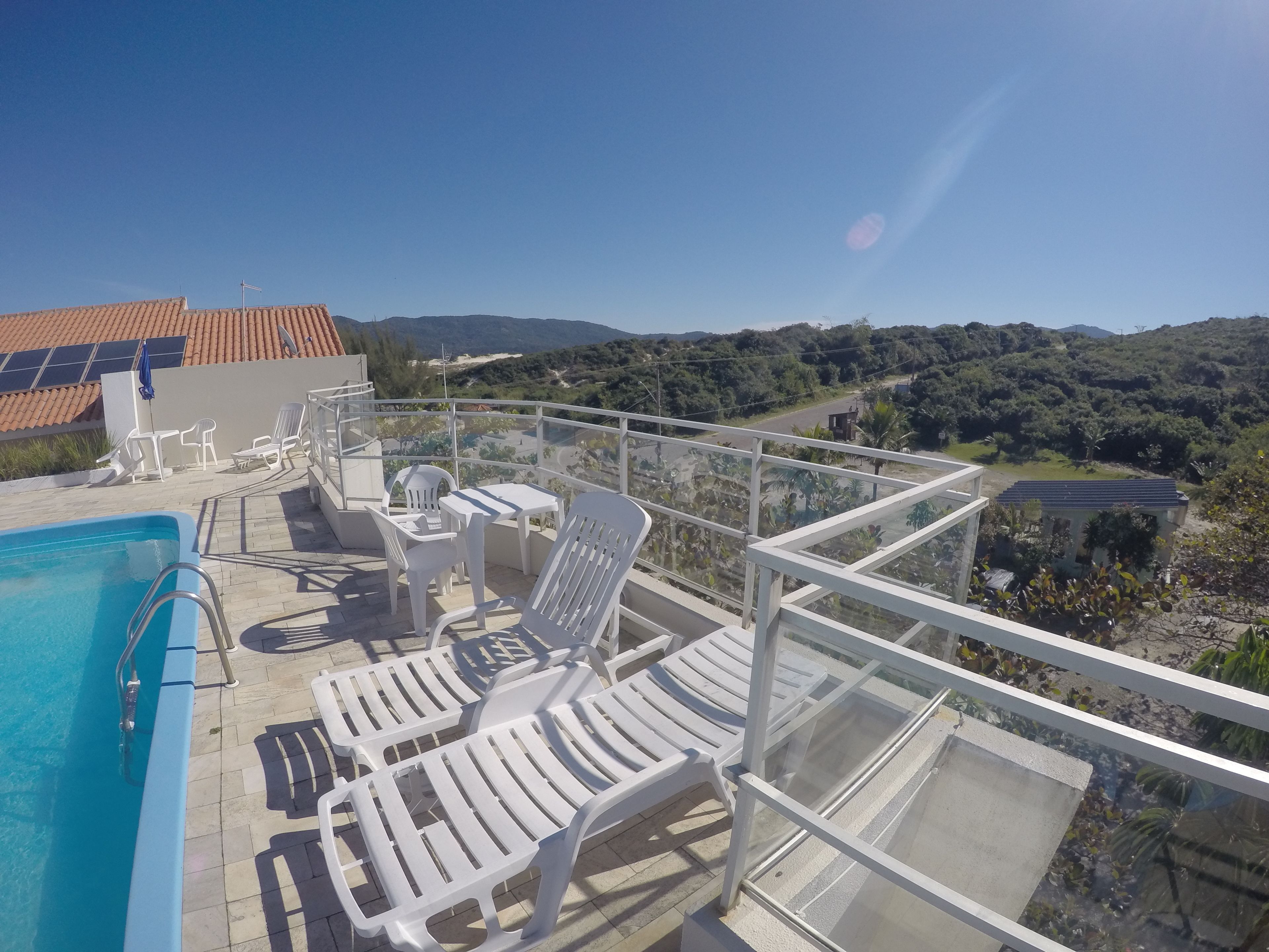 A poolside area with white lounge chairs and a table, overlooking a scenic landscape with hills and a clear sky.
