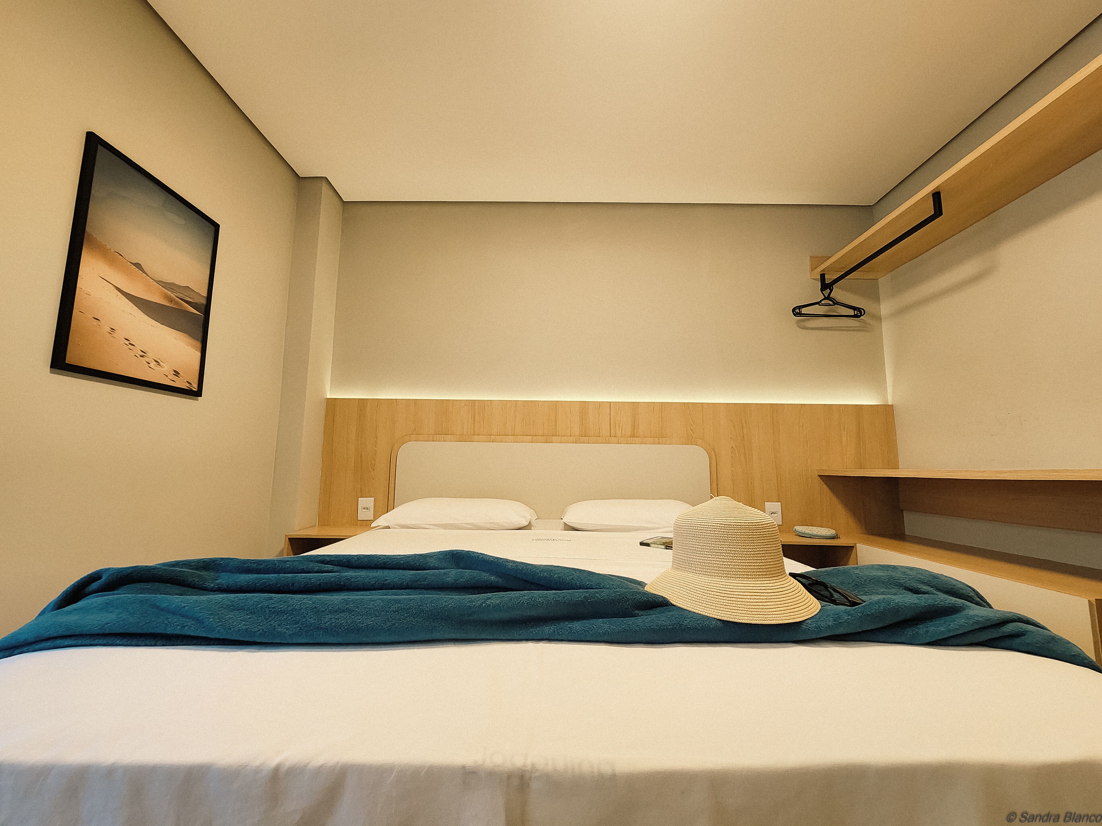 Ein Hotelzimmer mit Bett, Nachttisch, Wandregal und einem Gemälde.