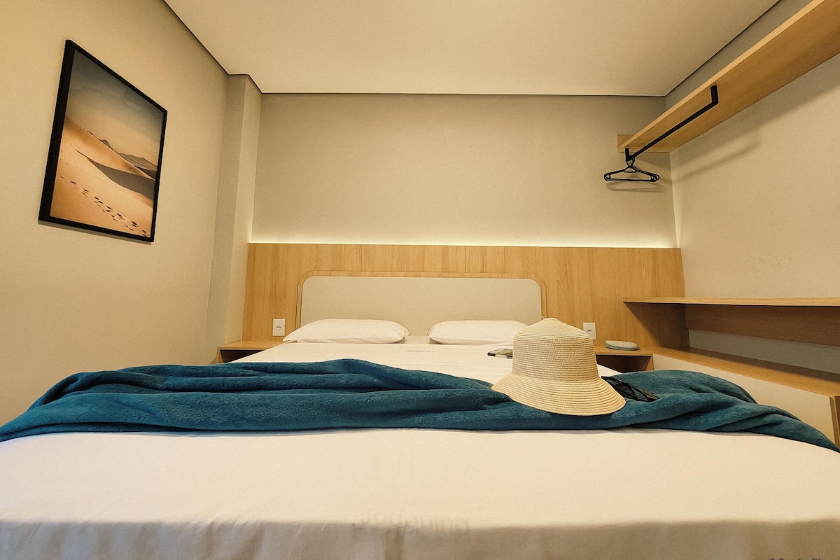 A hotel room with a bed, a nightstand, a wall-mounted shelf, and a painting.