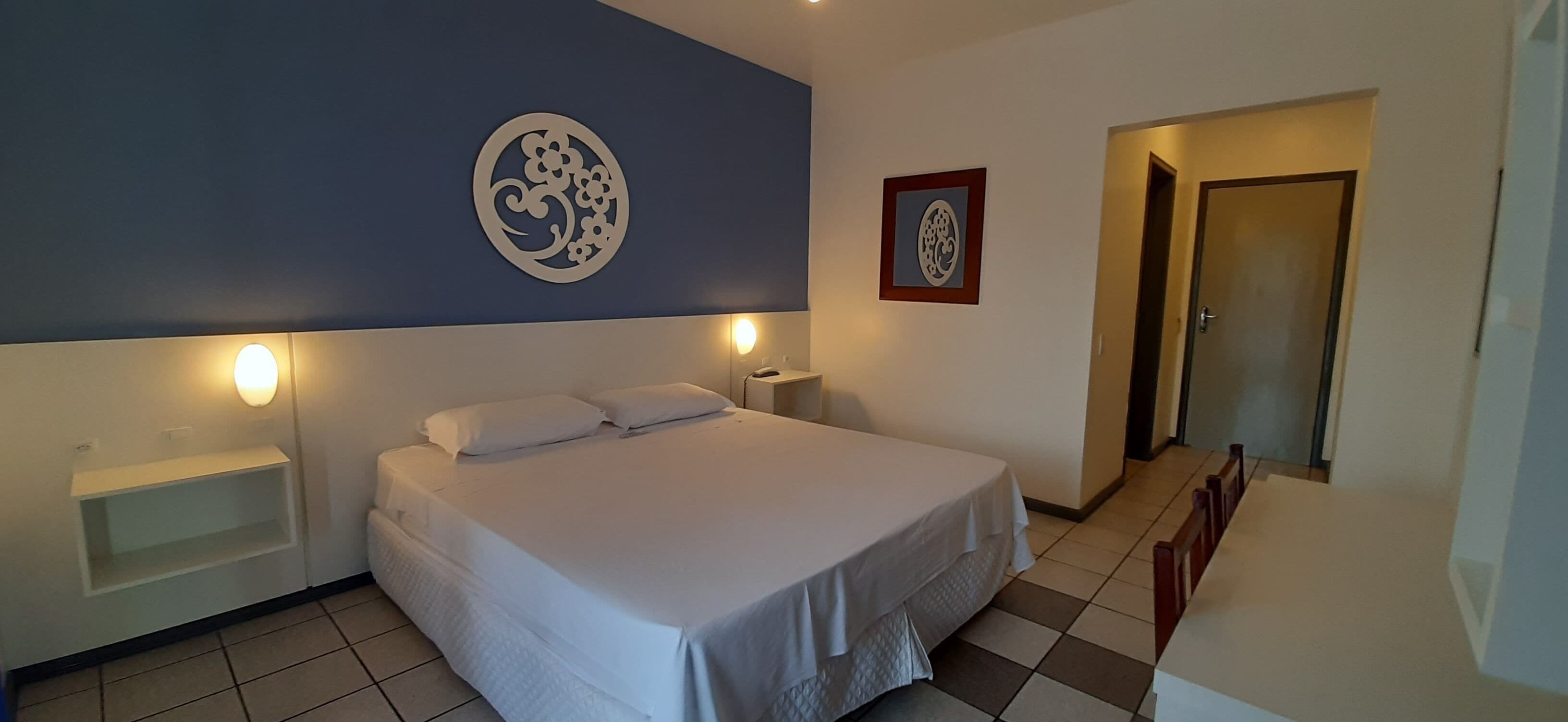 A bedroom with a bed, bedside tables, a wall decoration, and a door.