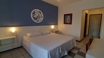 Um quarto com cama, mesas de cabeceira, um adorno na parede e uma porta.