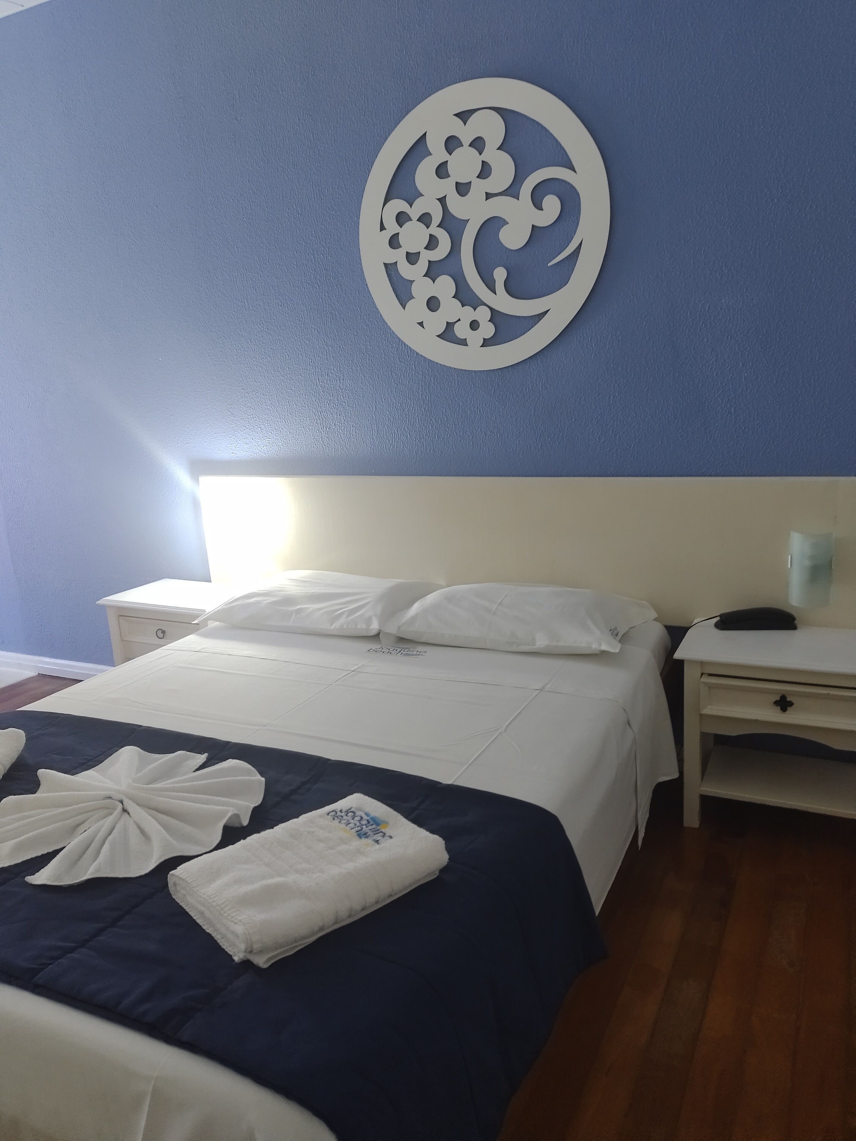 Una cama bien hecha con ropa de cama blanca, una pared azul con un diseño circular decorativo y un suelo de madera.