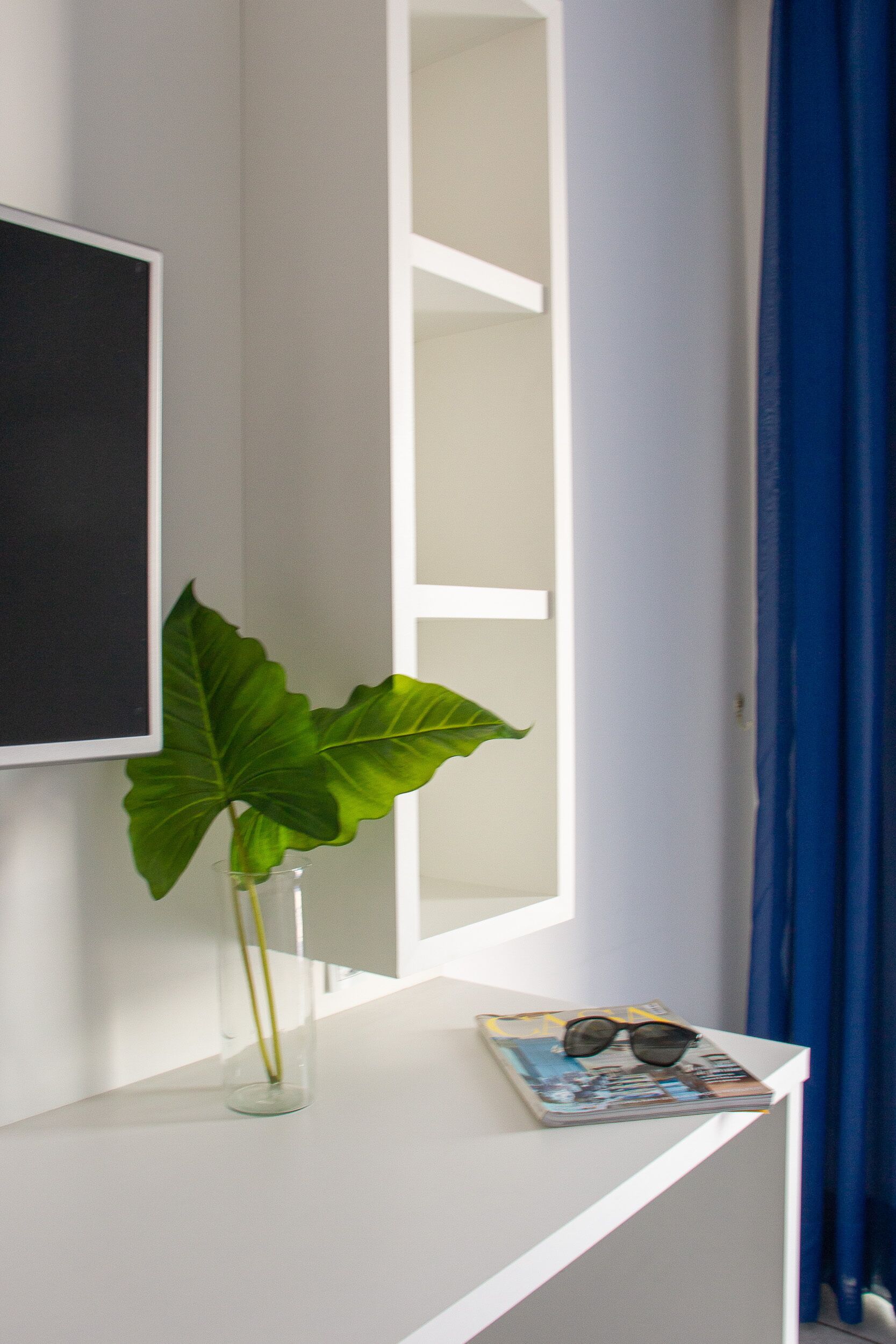 A white shelf with a clear vase containing a plant, a pair of glasses, and a magazine.