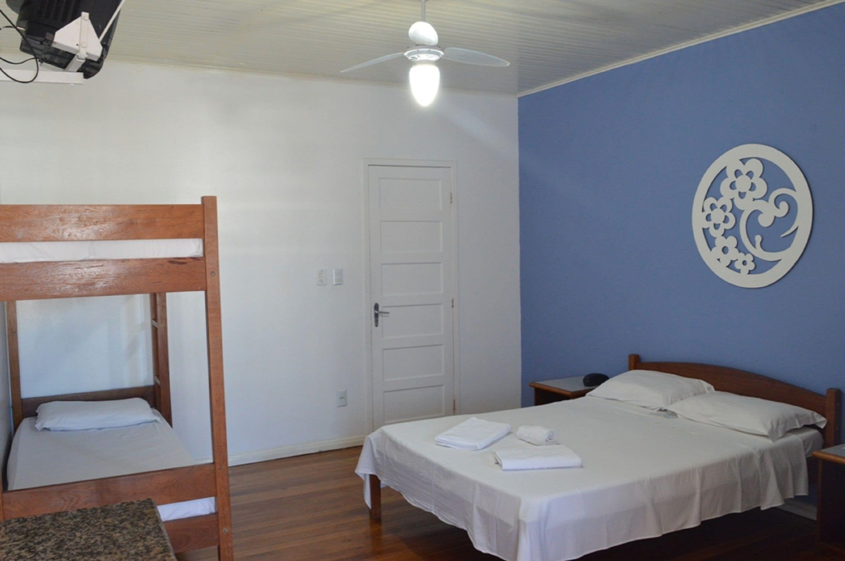 Una habitación con una cama individual, una litera, un ventilador de techo, una puerta y un adorno en la pared.