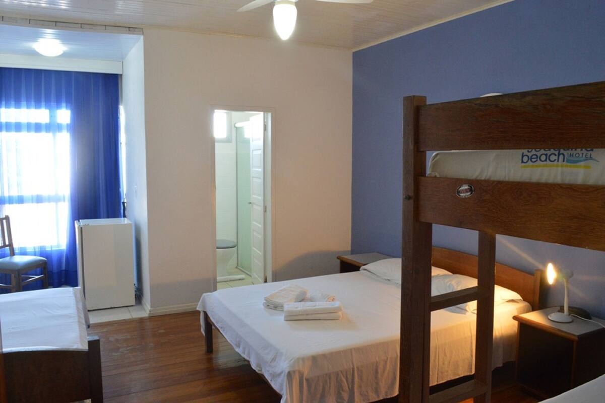 Hotelkamer met een stapelbed, een bureau met stoel, een klein tafeltje, een nachtkastje met lamp en een zichtbare badkamer door een geopende deur.