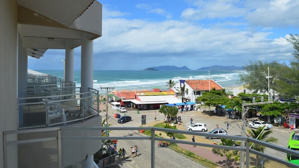 A coastal view from a balcony overlooking a beach area with a restaurant, cars, and a clear sky.