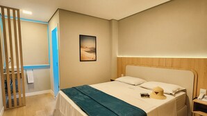 A hotel room with a bed, a nightstand, a wall-mounted lamp, and a door leading to another room.