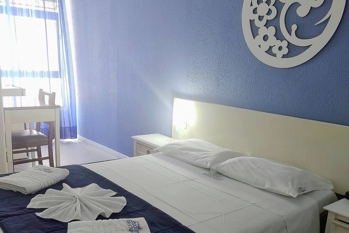 Een hotelkamer met een bed, nachtkastje, stoel en decoratieve wandversiering.