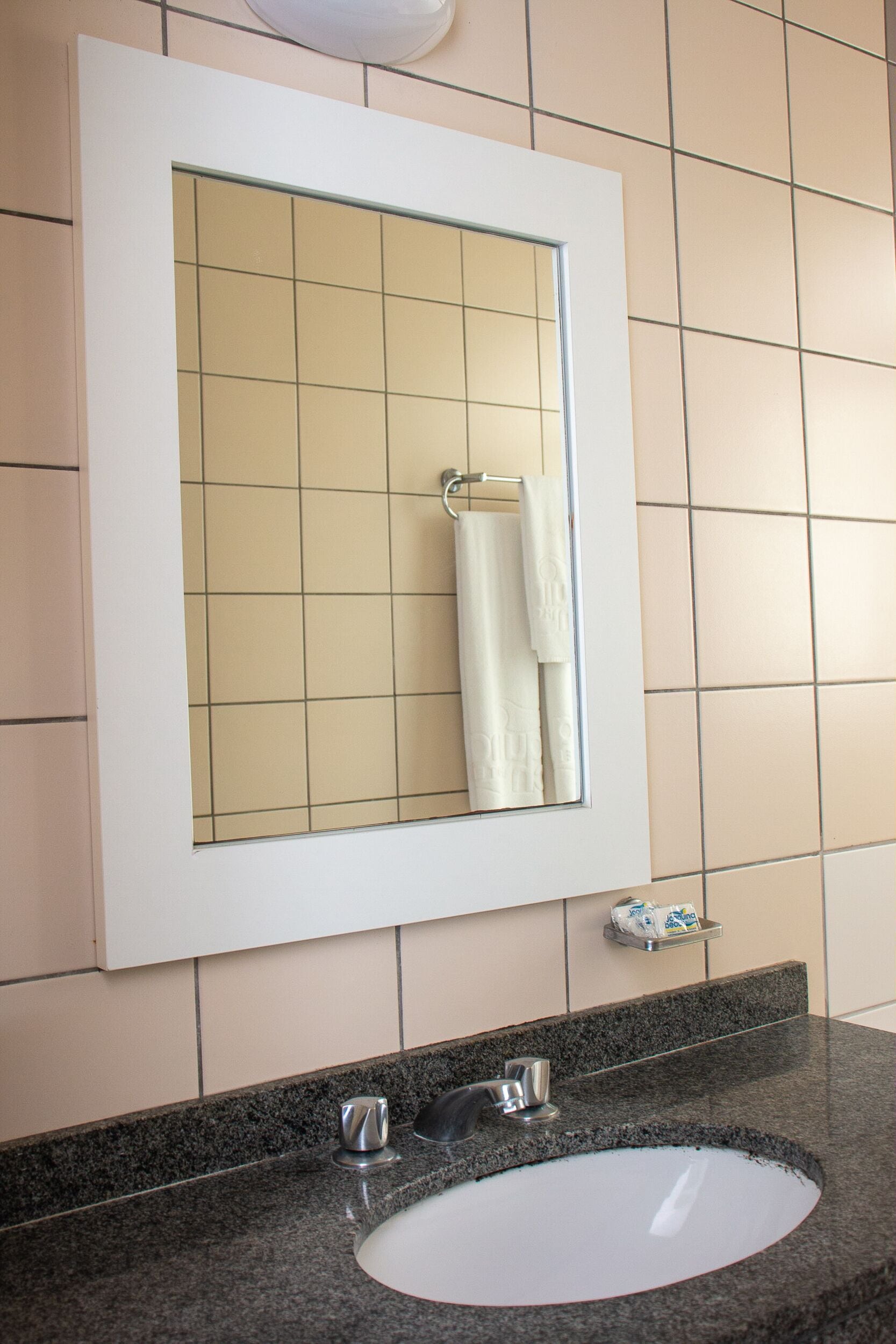 Un baño con un lavabo blanco, un espejo y una toalla colgada en un perchero.