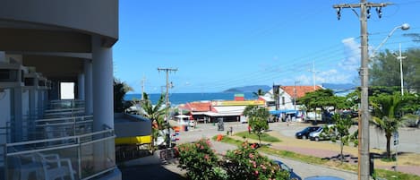 A coastal street with a restaurant, parked cars, and a building with a balcony.