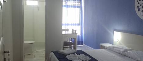A hotel room with a bed, a ceiling fan, a window with curtains, and a shower area.