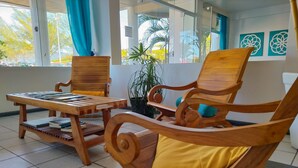 A wooden lounge area with chairs and a table, a potted plant, and a view of the outdoors.