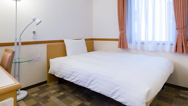 A hotel room with a bed, a desk with a lamp, a window with curtains, and a wall-mounted phone. - Toyoko Inn Shonan Hiratsuka Eki Kita Guchi No 1 (Hiratsuka)