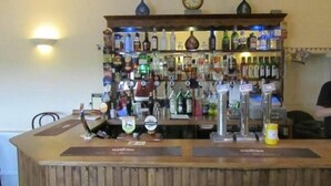 Zona de bar con mostrador de madera, diferentes botellas de licor y un reloj en la pared.