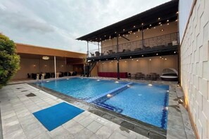 Ein Swimmingpool mit blauer Liegeauflage, einem überdachten Sitzbereich und einem Balkon mit Lichterketten.