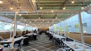 An indoor dining area with tables and chairs, large windows, and a high ceiling with exposed beams. - Riez Palace Hotel (East Tegal)